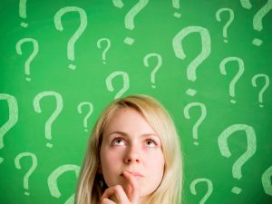Thinking woman in front of blackboard with question marks